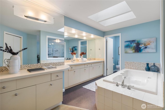 bathroom featuring a skylight, decorative backsplash, toilet, vanity, and a bath