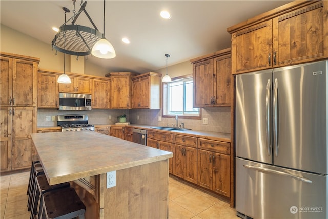 kitchen featuring appliances with stainless steel finishes, hanging light fixtures, vaulted ceiling, a kitchen island, and sink