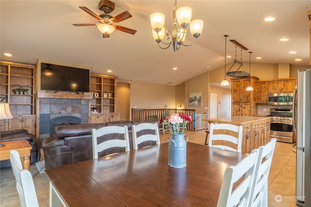 dining room with light tile patterned floors, lofted ceiling, ceiling fan with notable chandelier, and a tile fireplace