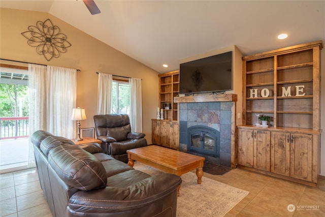 living room with ceiling fan, vaulted ceiling, a fireplace, and light tile patterned flooring