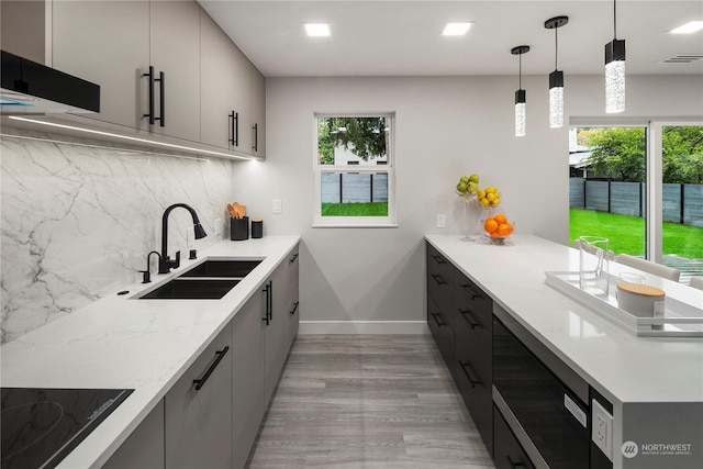 kitchen with sink, light stone counters, decorative light fixtures, a wealth of natural light, and decorative backsplash