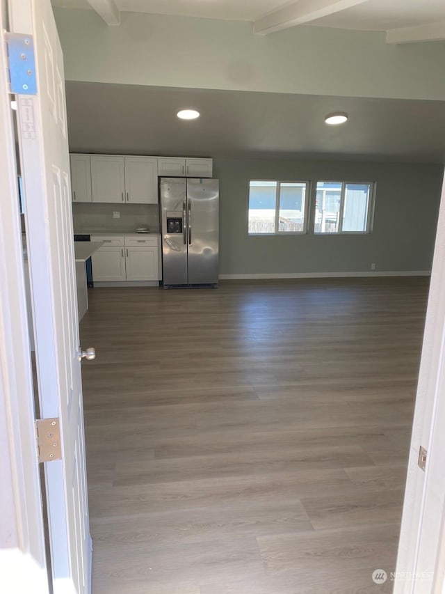 kitchen with white cabinets, light wood-type flooring, beam ceiling, and stainless steel fridge