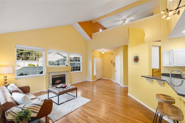 living room featuring light hardwood / wood-style floors, high vaulted ceiling, beam ceiling, and ceiling fan