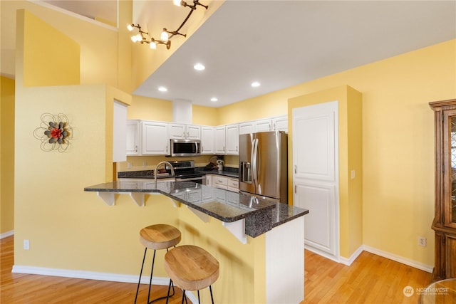 kitchen featuring appliances with stainless steel finishes, white cabinetry, a kitchen breakfast bar, kitchen peninsula, and light wood-type flooring