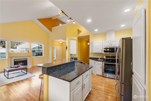 kitchen featuring white cabinetry, stainless steel appliances, vaulted ceiling with beams, sink, and a breakfast bar area