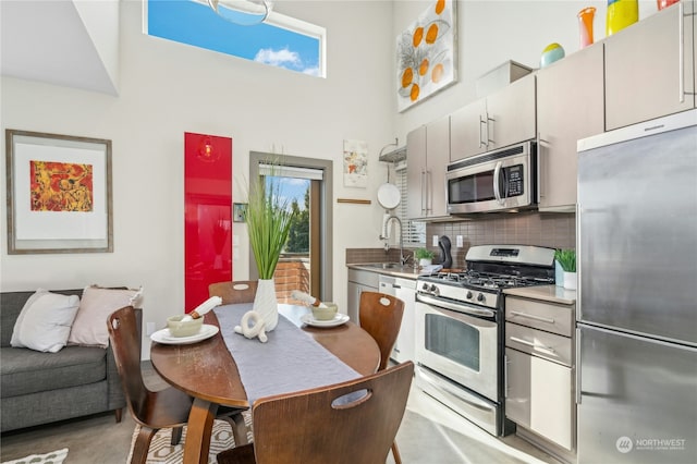 kitchen with stainless steel appliances, sink, backsplash, and a towering ceiling