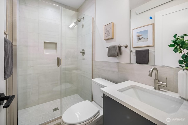 bathroom with a shower with door, vanity, tile walls, and toilet