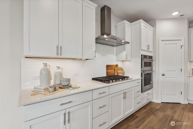 kitchen featuring stainless steel appliances, dark hardwood / wood-style floors, white cabinets, decorative backsplash, and wall chimney exhaust hood