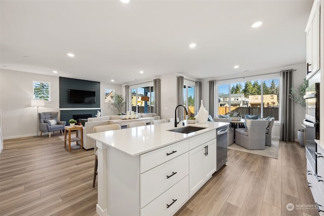 kitchen with white cabinetry, a large fireplace, sink, and an island with sink