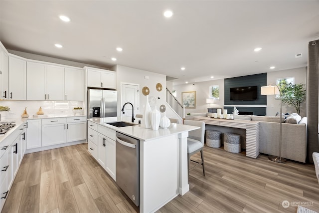 kitchen with white cabinetry, sink, stainless steel appliances, and an island with sink