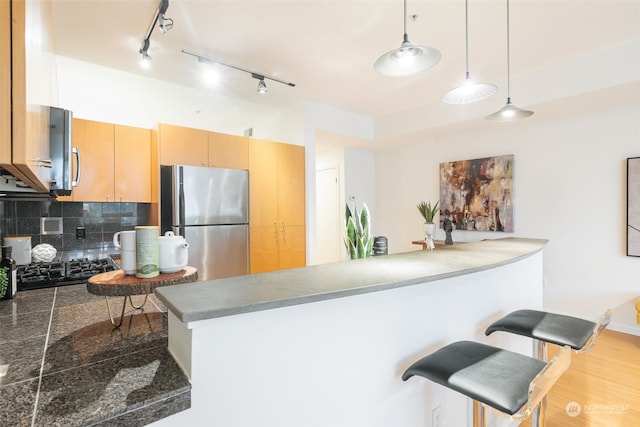 kitchen featuring pendant lighting, appliances with stainless steel finishes, tasteful backsplash, kitchen peninsula, and a breakfast bar area