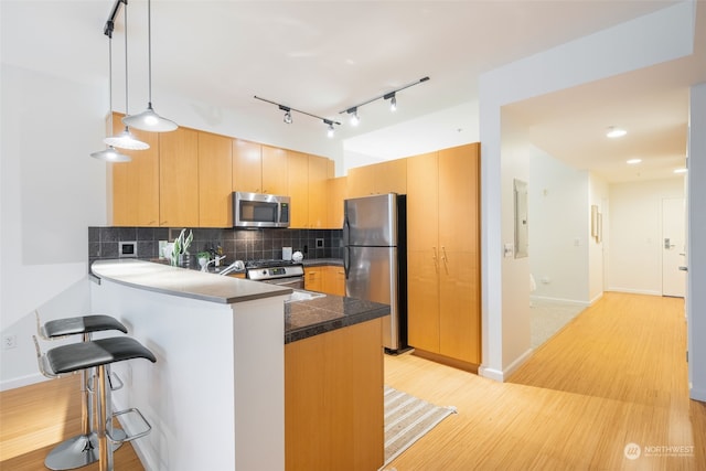 kitchen featuring backsplash, pendant lighting, kitchen peninsula, light wood-type flooring, and appliances with stainless steel finishes