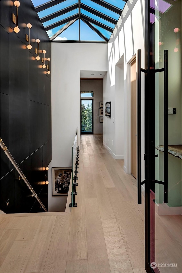 hall featuring high vaulted ceiling, wood-type flooring, and a skylight