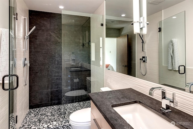 bathroom featuring toilet, tile walls, a shower with door, and vanity