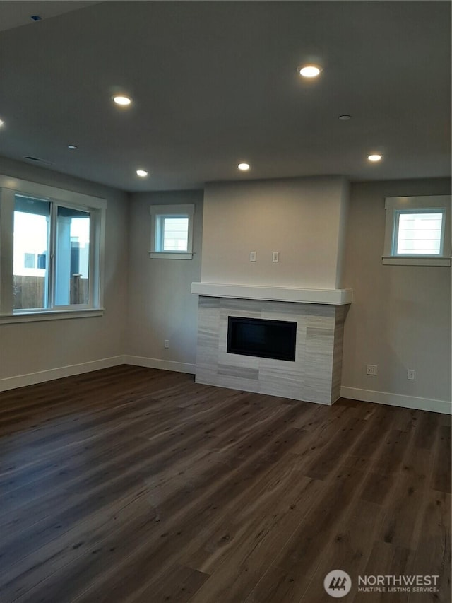 unfurnished living room with dark wood finished floors, a wealth of natural light, and a tile fireplace