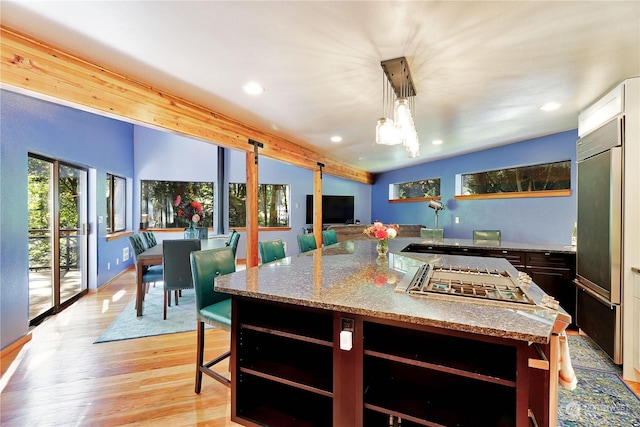 kitchen with a center island, hanging light fixtures, paneled fridge, light wood-type flooring, and light stone counters