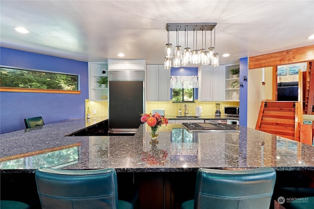 kitchen with appliances with stainless steel finishes, a kitchen breakfast bar, dark stone counters, white cabinets, and sink