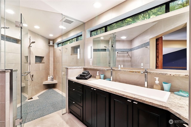 bathroom with tile patterned flooring, tile walls, walk in shower, and vanity