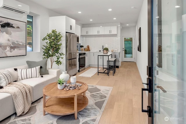 living room with sink, a wall mounted AC, and light hardwood / wood-style floors