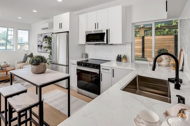 kitchen featuring sink, white cabinetry, an AC wall unit, appliances with stainless steel finishes, and a healthy amount of sunlight