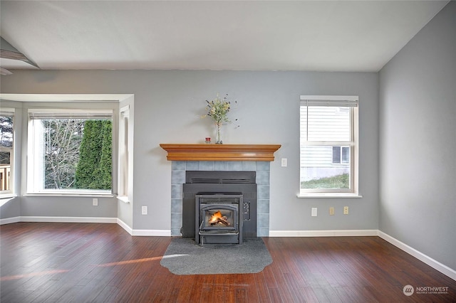 unfurnished living room with lofted ceiling, a healthy amount of sunlight, dark hardwood / wood-style flooring, and a wood stove