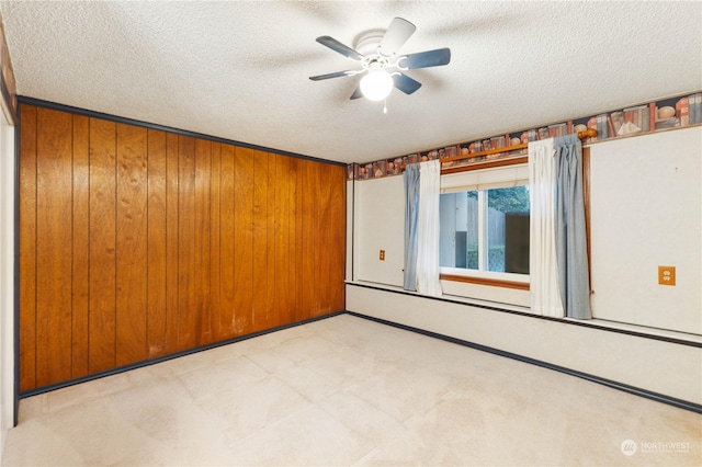 unfurnished room with ceiling fan, wooden walls, and a textured ceiling