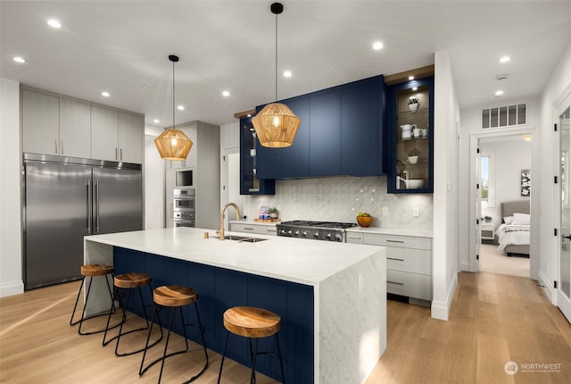 kitchen with pendant lighting, appliances with stainless steel finishes, tasteful backsplash, an island with sink, and blue cabinets