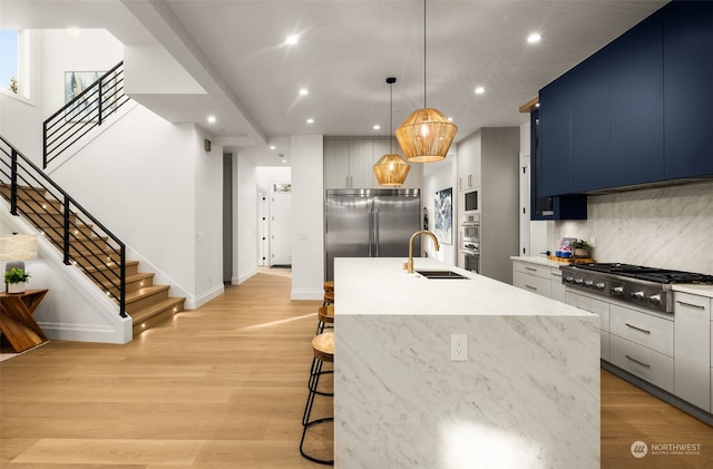 kitchen featuring appliances with stainless steel finishes, sink, decorative light fixtures, blue cabinets, and a center island with sink