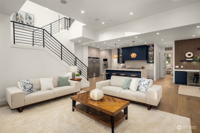 living room featuring light hardwood / wood-style floors, a high ceiling, beverage cooler, and bar