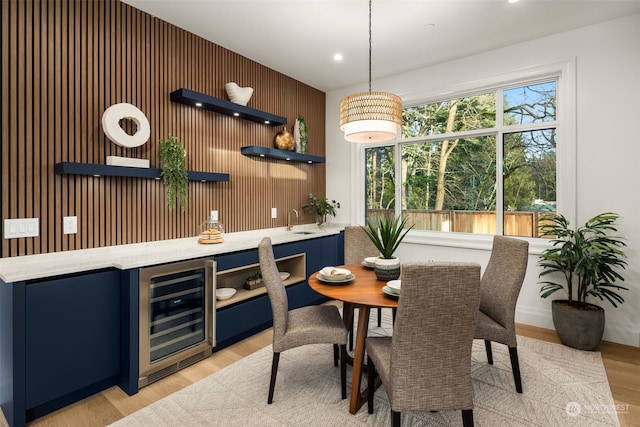 dining area featuring light wood-type flooring, wood walls, wine cooler, and indoor wet bar