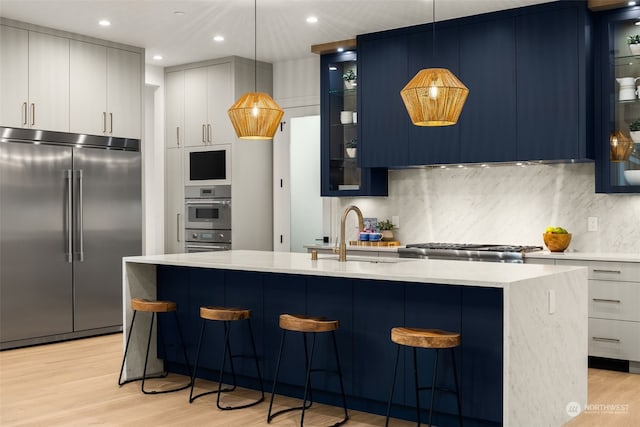 kitchen with built in fridge, an island with sink, pendant lighting, and sink