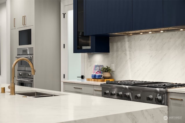 kitchen with light stone countertops, decorative backsplash, blue cabinets, sink, and double oven