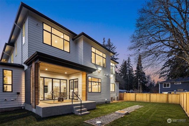 back house at dusk with a lawn and a patio