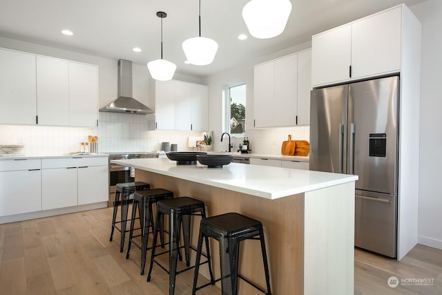 kitchen featuring white cabinetry, a center island, wall chimney exhaust hood, and stainless steel refrigerator with ice dispenser