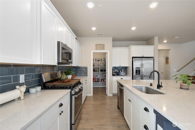 kitchen featuring white cabinetry, appliances with stainless steel finishes, sink, and light stone counters