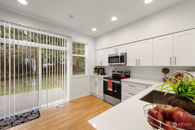 kitchen with light hardwood / wood-style flooring, stainless steel appliances, and white cabinets