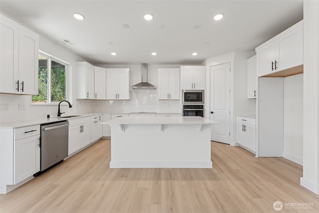 kitchen with stainless steel dishwasher, a kitchen island, oven, light wood-type flooring, and wall chimney exhaust hood