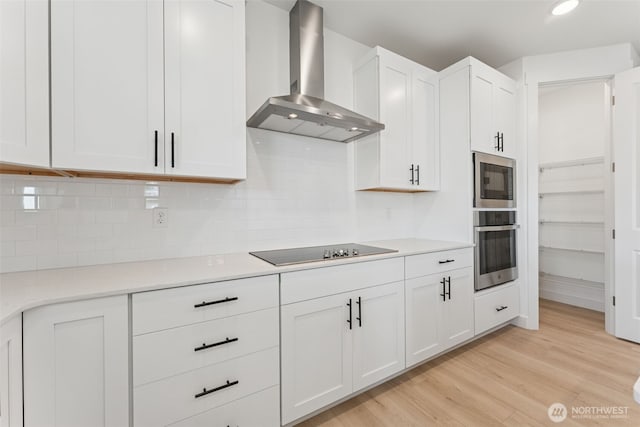 kitchen featuring wall chimney range hood, white cabinets, black electric stovetop, light wood finished floors, and light countertops