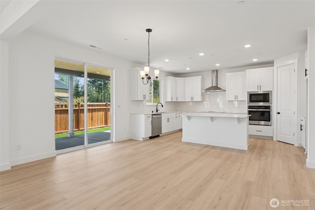 kitchen featuring decorative backsplash, appliances with stainless steel finishes, a sink, light countertops, and wall chimney exhaust hood