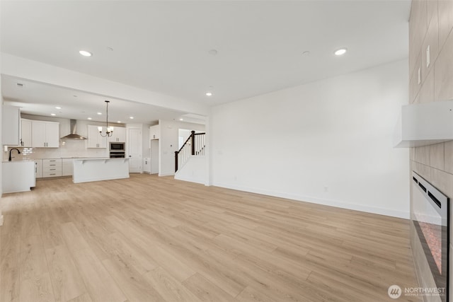 unfurnished living room with a fireplace, stairs, a sink, light wood finished floors, and recessed lighting