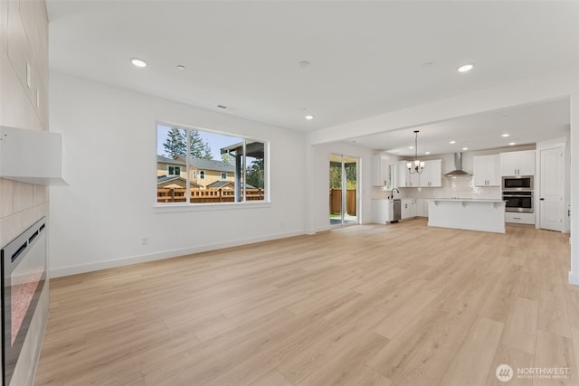 unfurnished living room featuring light wood finished floors, a chandelier, a tiled fireplace, recessed lighting, and baseboards