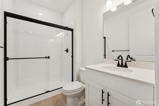 bathroom with vanity, a stall shower, toilet, and wood finished floors