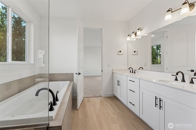 full bath with a relaxing tiled tub, a sink, and a healthy amount of sunlight
