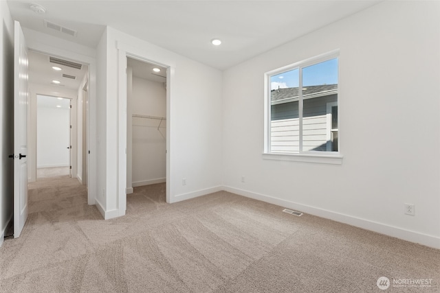 unfurnished bedroom with carpet floors, baseboards, a walk in closet, and visible vents