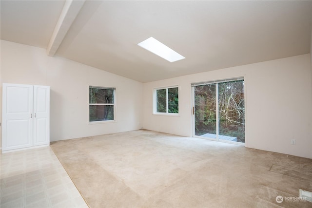 carpeted empty room with vaulted ceiling with skylight