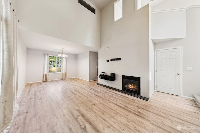 unfurnished living room featuring light hardwood / wood-style floors, a chandelier, and a towering ceiling