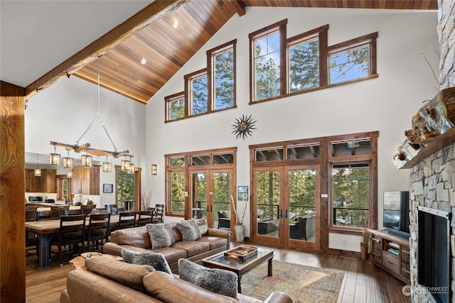 living room featuring hardwood / wood-style floors, a stone fireplace, vaulted ceiling with beams, and french doors