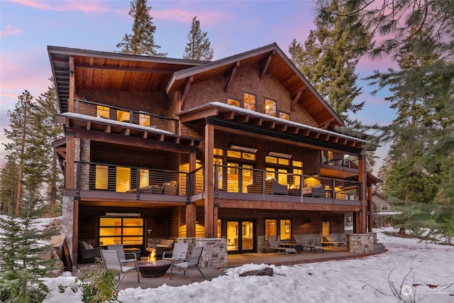 snow covered back of property with a patio, a balcony, and an outdoor fire pit