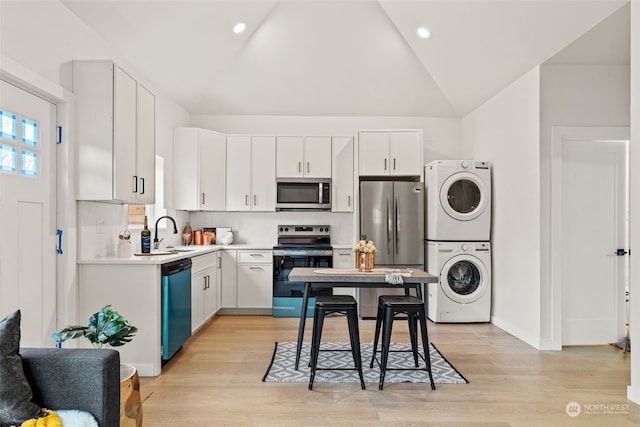 kitchen with lofted ceiling, sink, appliances with stainless steel finishes, stacked washer / dryer, and white cabinets