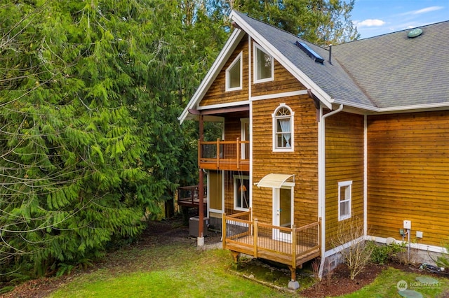 rear view of property with a balcony, a deck, central AC unit, and a lawn